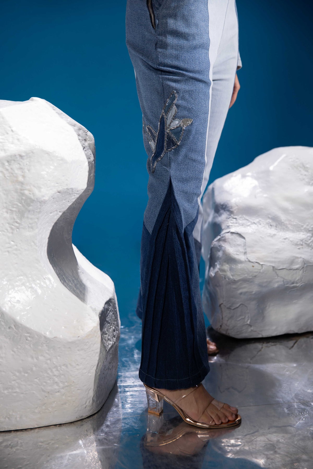 Close-up of Fearless Ferð Denim Jumpsuit showing one-shoulder silhouette, bell sleeve, flared leg and Ferð patchwork